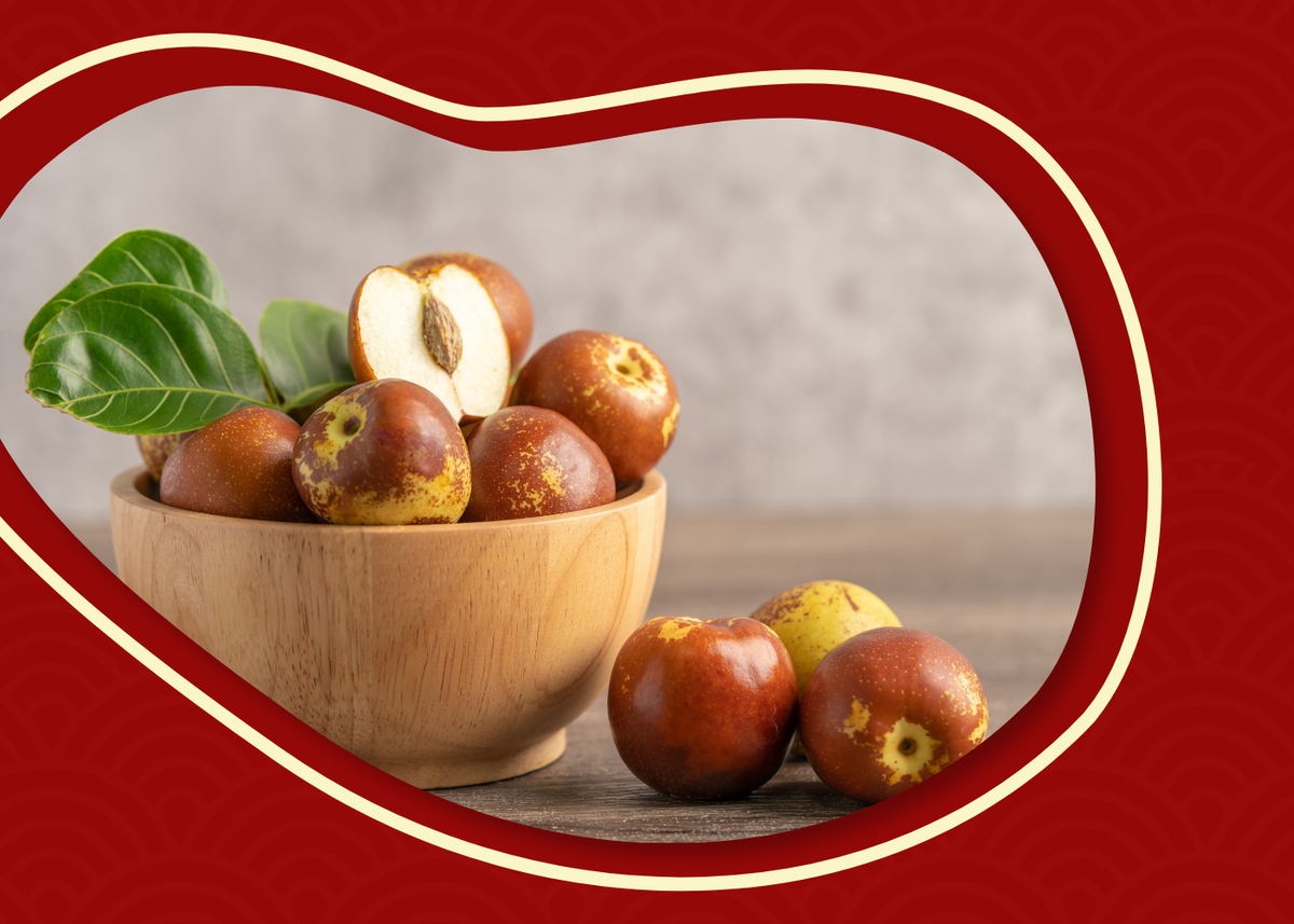 Fresh Royal Jujubes in a wooden bowl with glossy leaves and a sliced jujube showing the crisp white flesh inside.