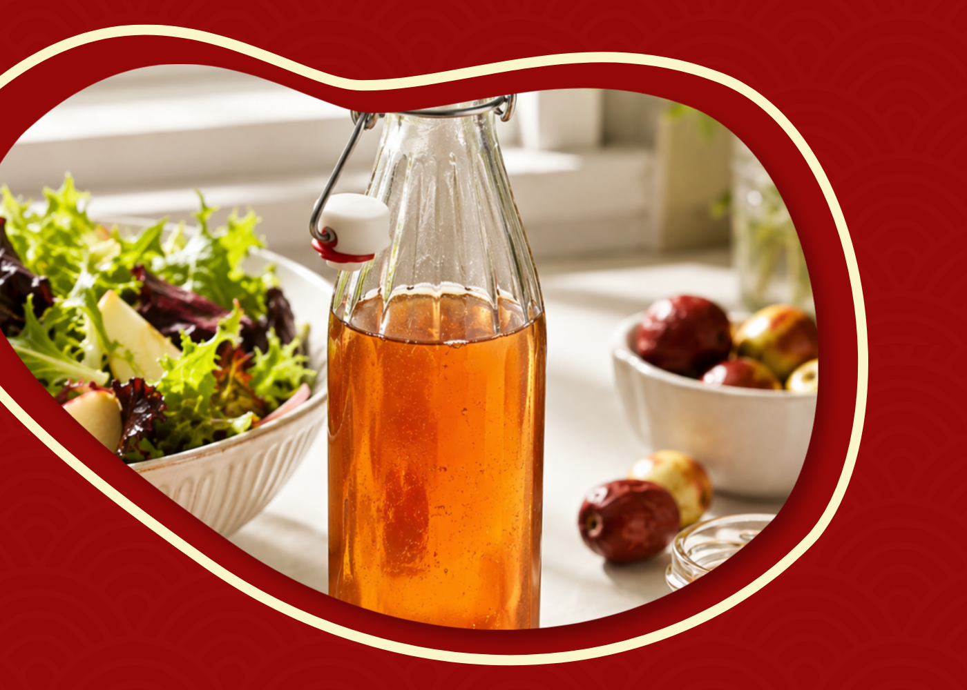 Clear glass bottle of amber jujube vinegar with salad dressing ingredients in a bright kitchen setting.